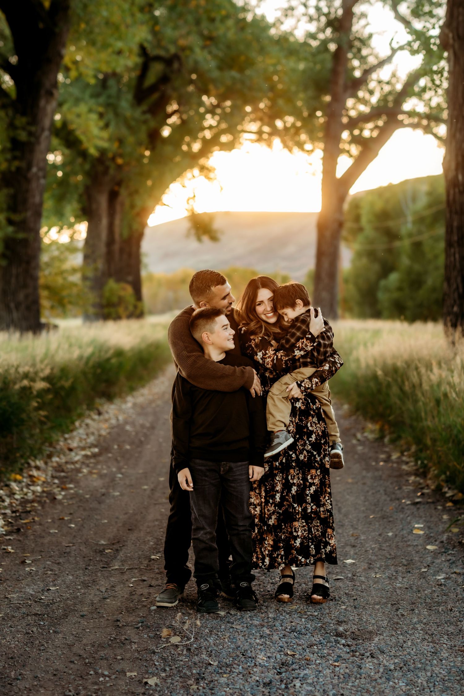 A couple shares a tender moment at sunset on a tree-lined dirt path during a romantic photoshoot.