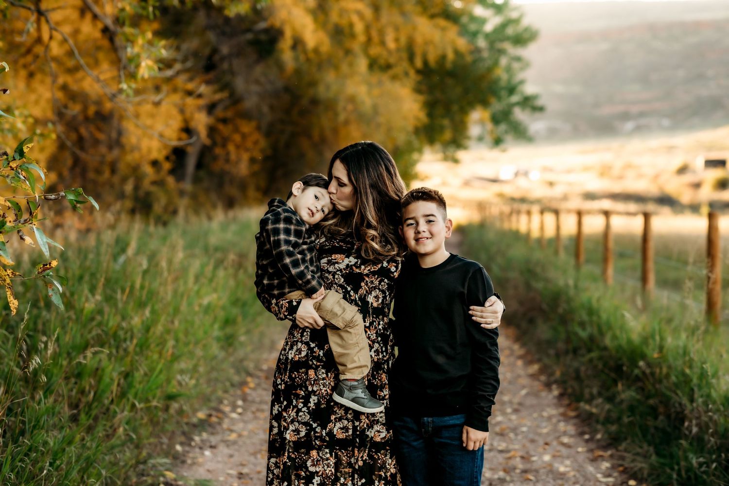 A couple embraces on a scenic autumn path surrounded by golden trees and warm sunlight.