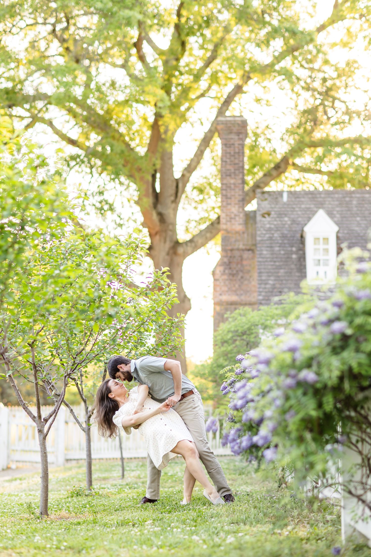 Couple doing a dip in a cottage garden with wisteria blooming during their engagement portrait photography session in Colonial Williamsburg.