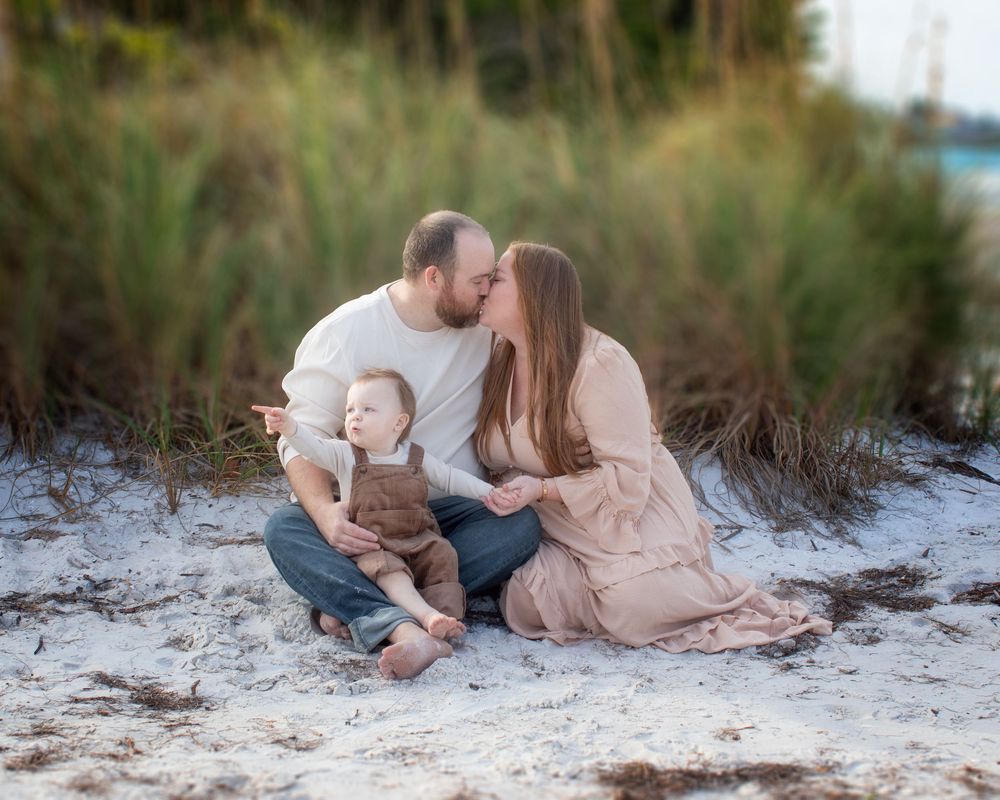 Family sitting together on a sandy beach at sunset wearing coordinated neutral colored outfits.