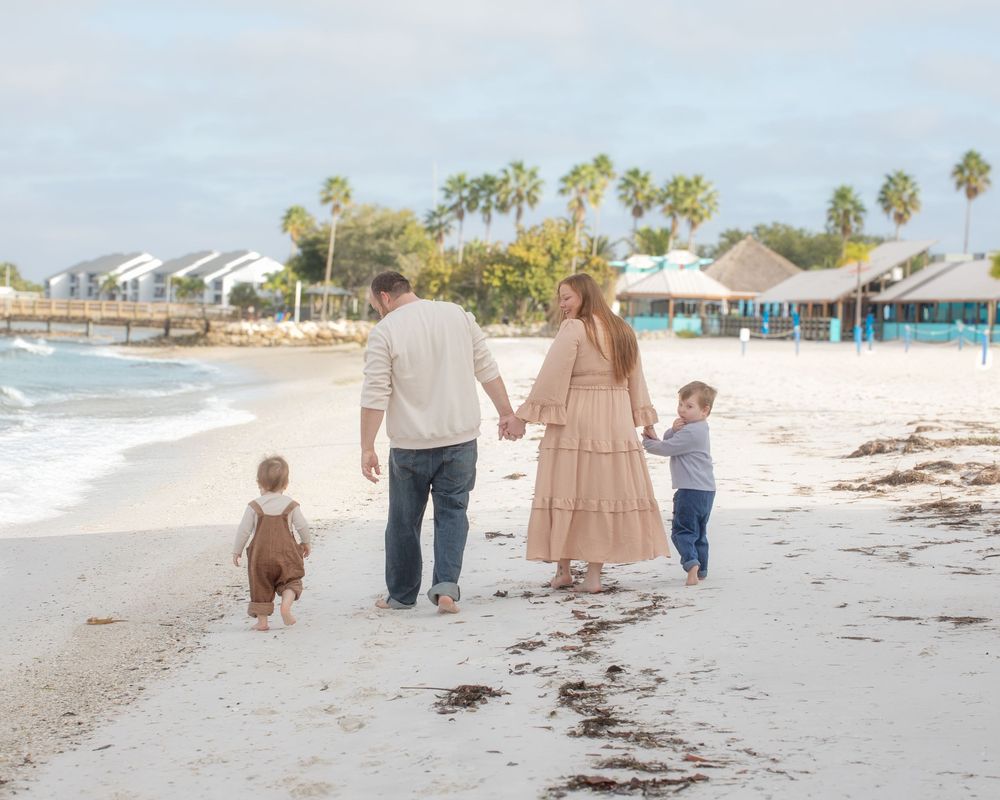 A family strolls hand in hand on a peaceful beach shoreline during a sunny day.