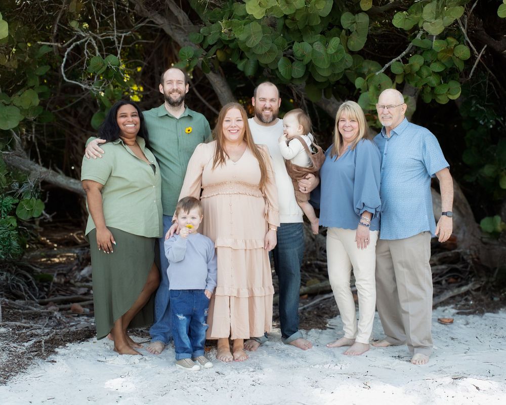 A group of people wearing coordinated pastel outfits pose together on a white sandy beach for family photos.