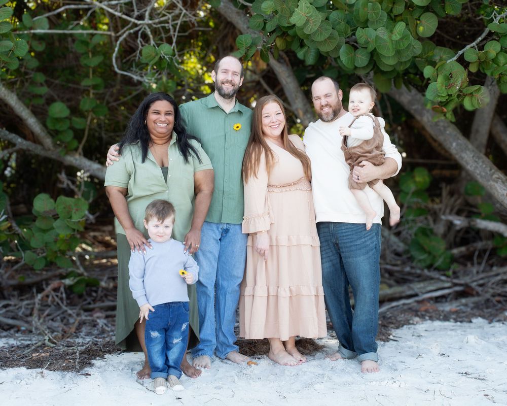 Group portrait on beach with lush greenery and natural lighting.