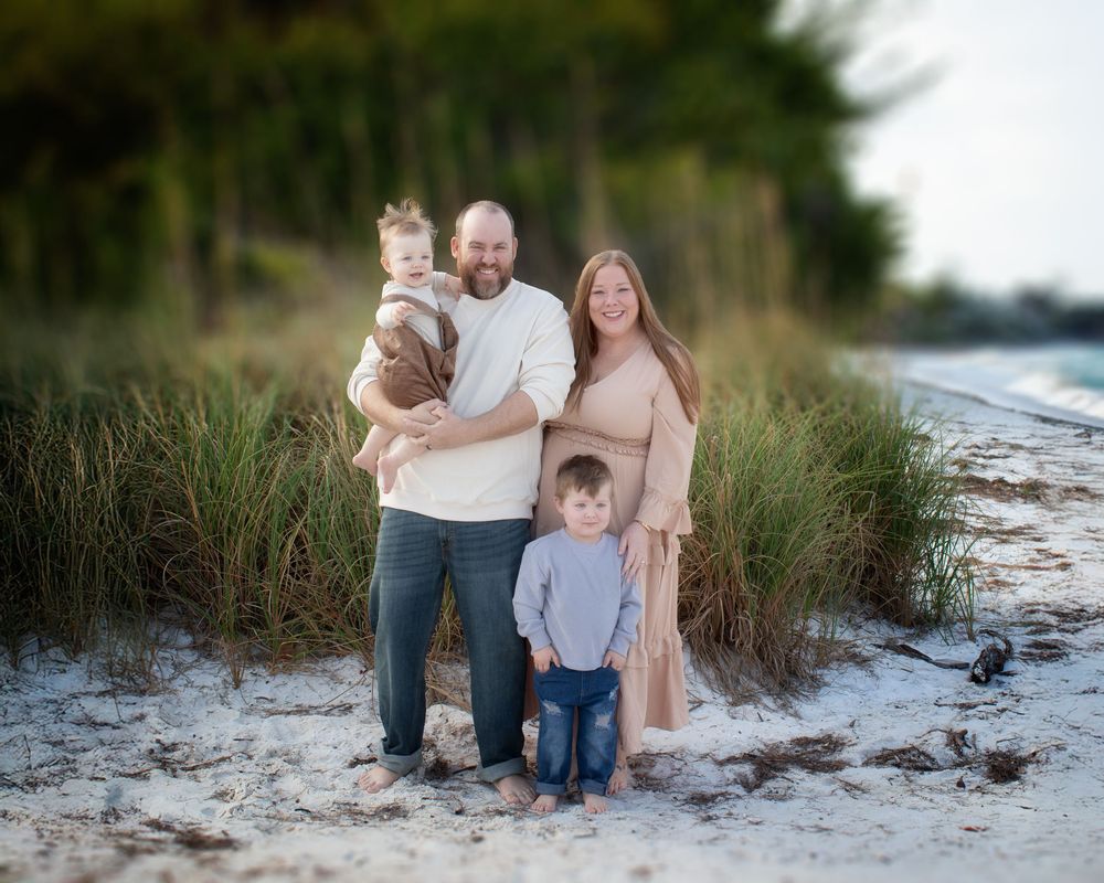 Family enjoying a sunset photoshoot together on a sandy beach with sea grass and dunes in the background.