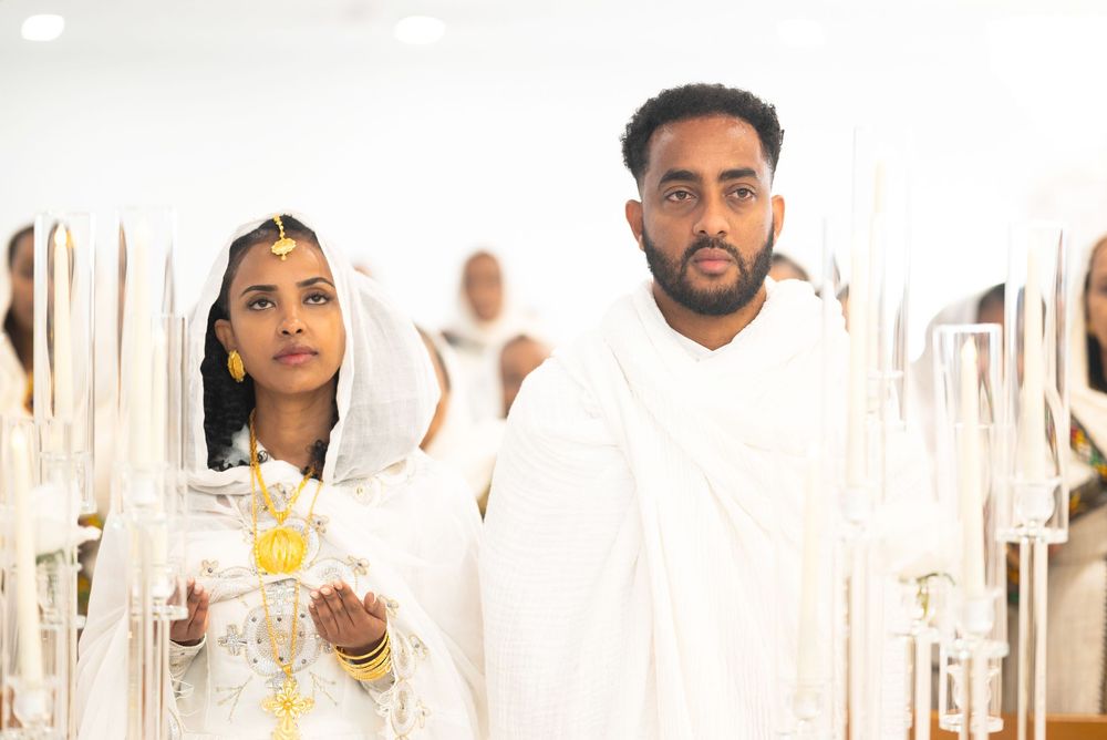 Ethiopian bride and groom in traditional white habesha kemis and netela walking ceremonially with gold jewelry.