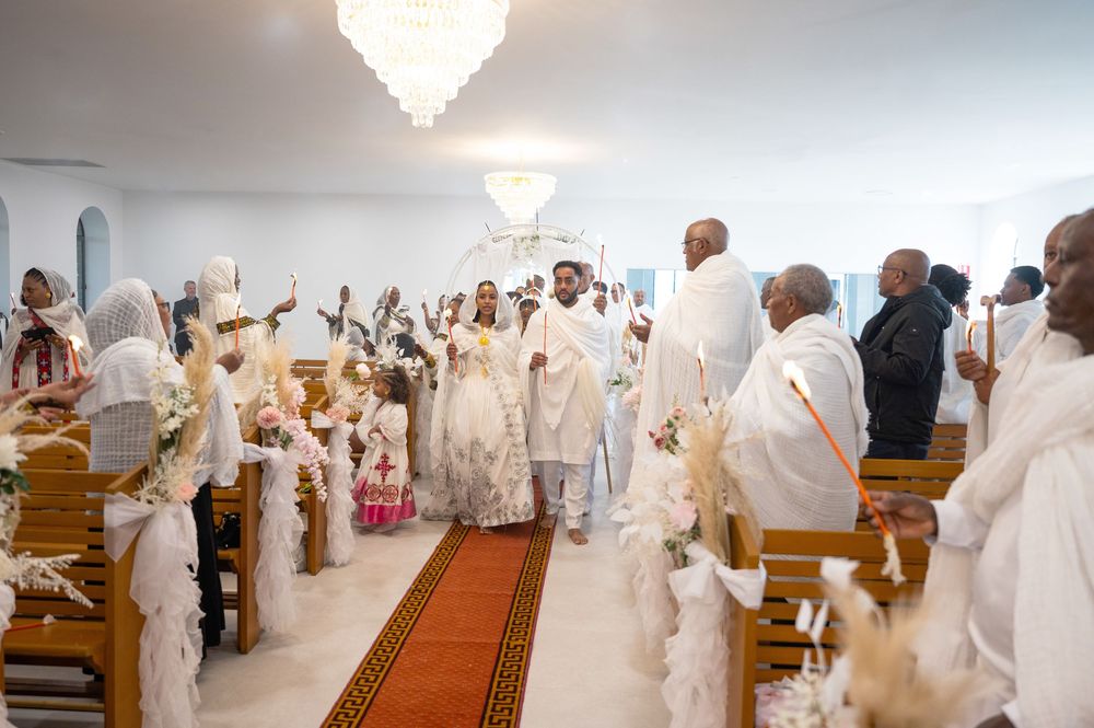 Ethiopian Orthodox wedding procession down church aisle with guests in white traditional garments.