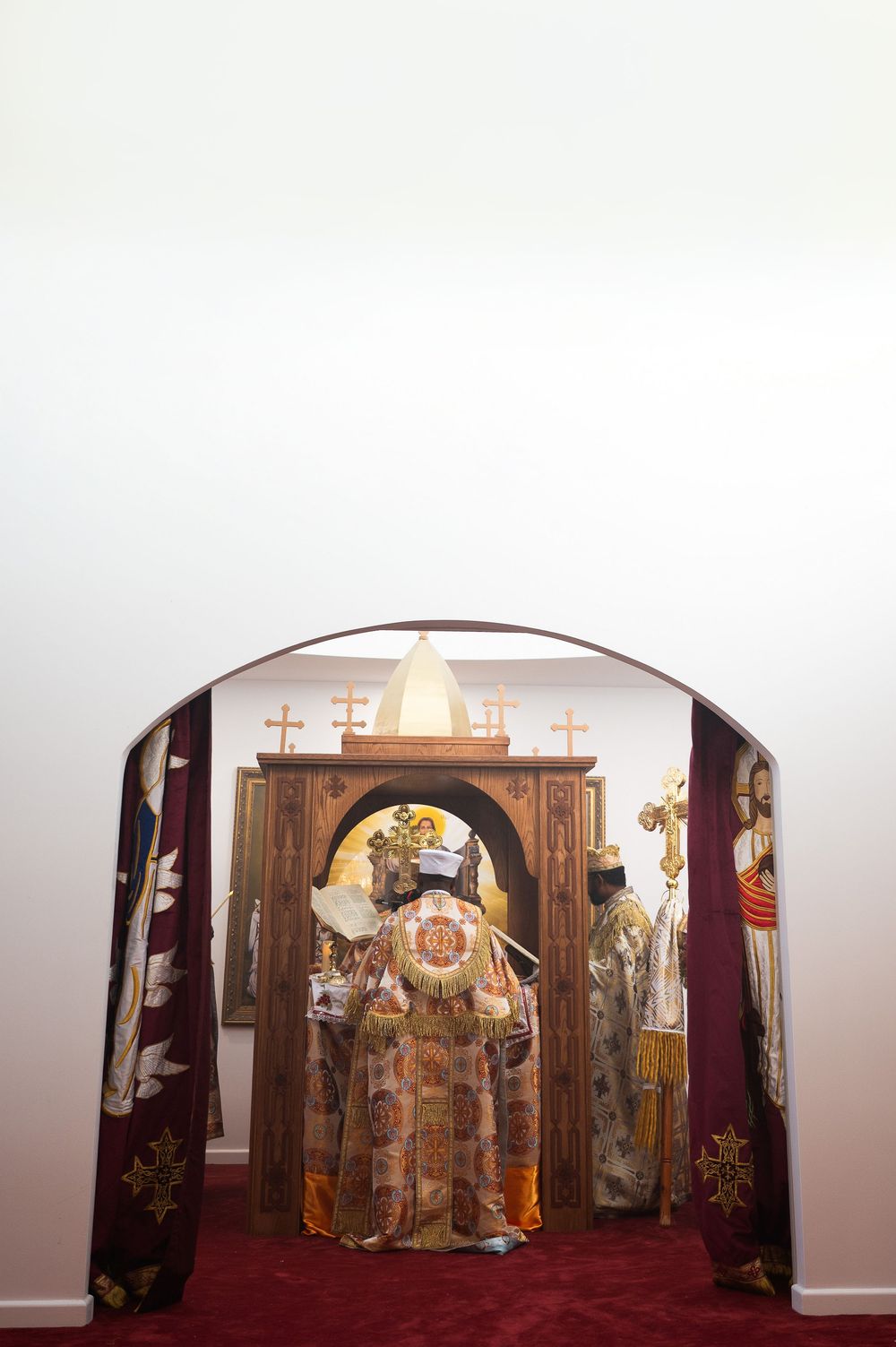 Ethiopian Orthodox priest in elaborate golden vestments standing before ornate wooden altar with crosses.
