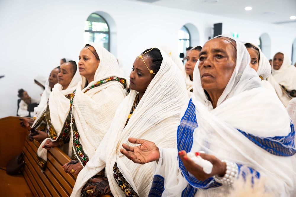 Ethiopian Orthodox women in white shawls with blue trim praying devoutly in church pews.