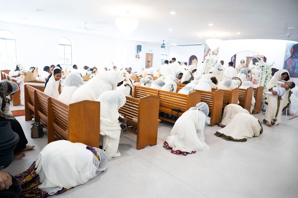 Ethiopian Orthodox congregation bowing in deep prayer prostrated over wooden church pews.