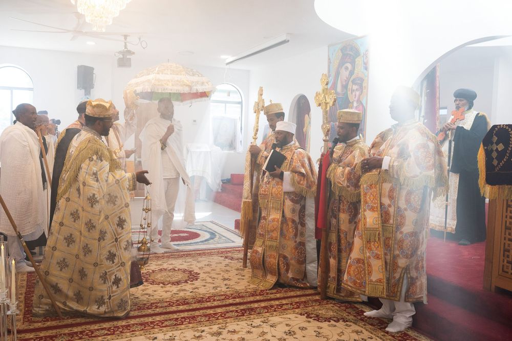 Ethiopian Orthodox clergy in golden vestments performing sacred ritual with ceremonial umbrella in church.