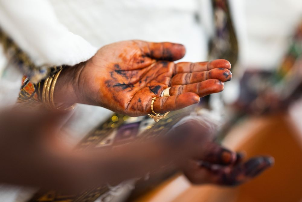 Close-up of hands adorned with henna mehndi and gold bangles at an Ethiopian wedding ceremony.