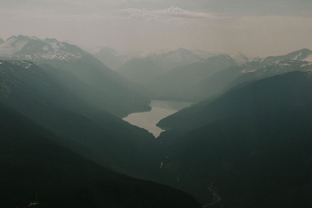 Panoramic view of misty mountain ranges and fjords under an overcast sky in moody tones.