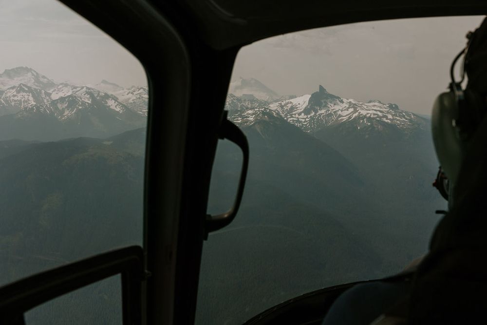 Silhouetted mountain peaks against a misty sky viewed through a helicopter window.