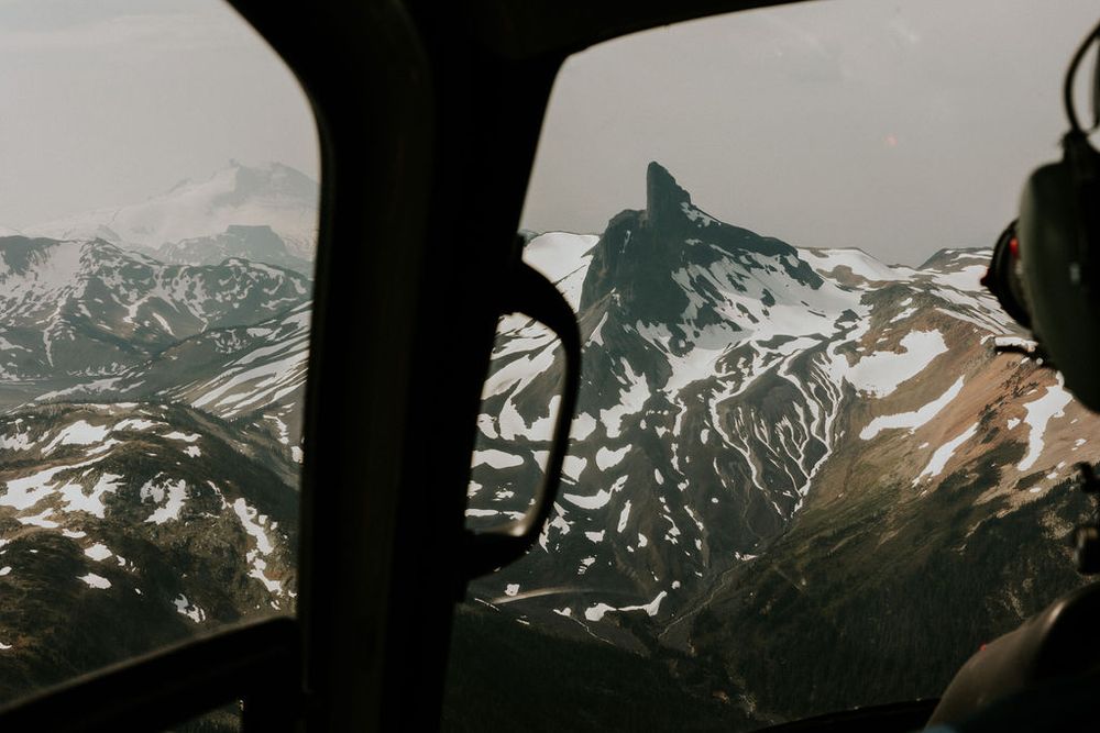 Panoramic view of rugged mountain ranges with snow patches seen through a vehicle window frame.