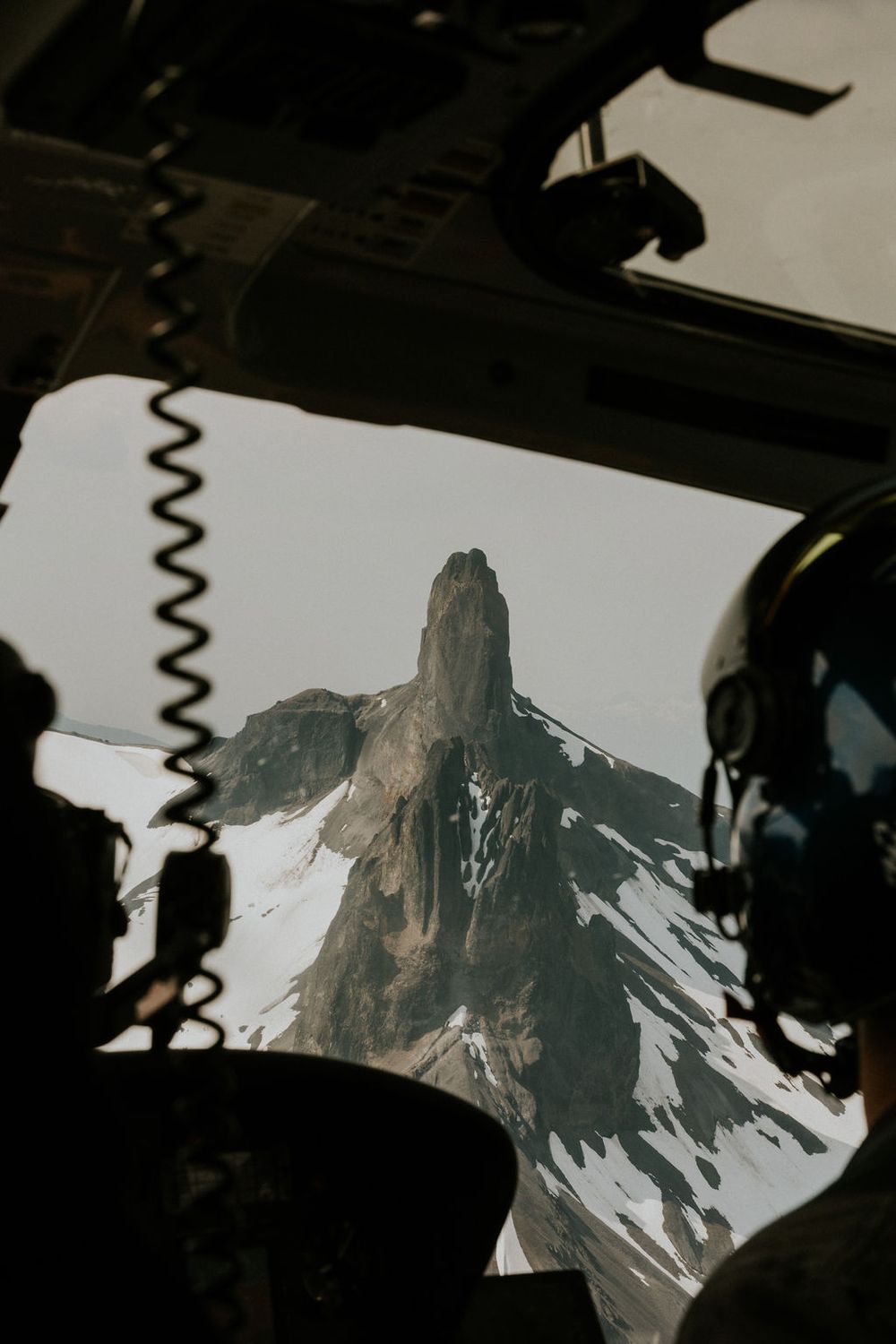 View of snow-capped mountain peaks through an aircraft window with silhouettes in the foreground.