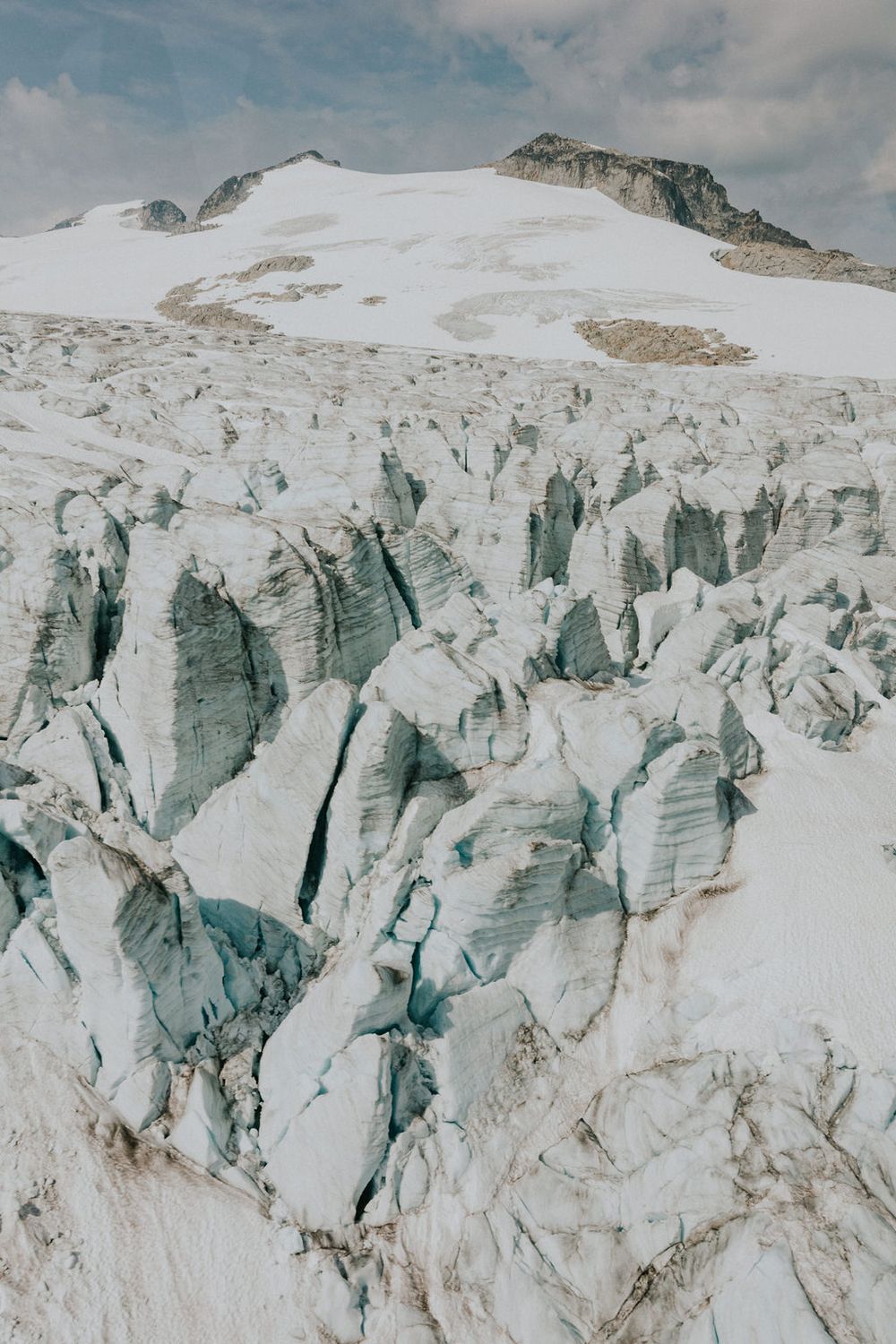 Dramatic view of a crevassed glacier with jagged ice formations and snow-covered mountain peaks in the background.