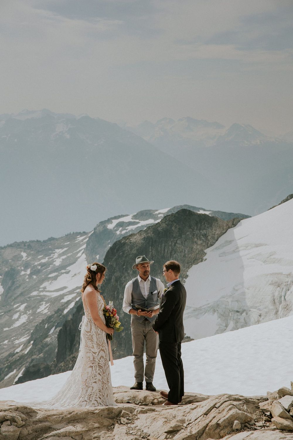 A wedding ceremony takes place on a snowy mountain peak with dramatic views of snow-capped peaks in the background.