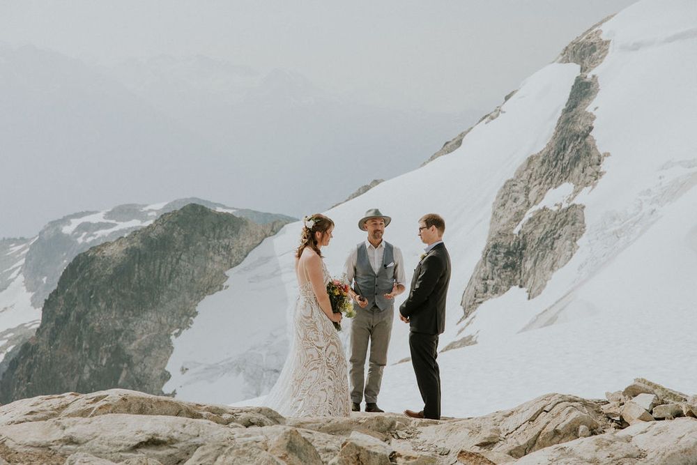A scenic mountain wedding ceremony takes place on a snowy peak with dramatic mountain vistas in the background.