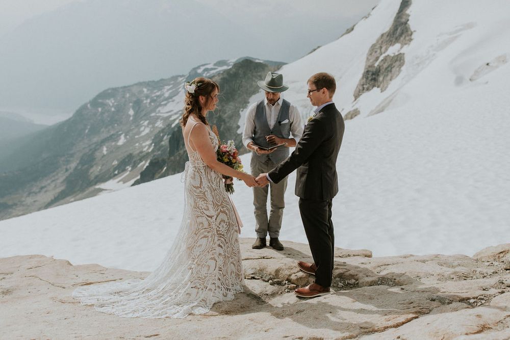 An intimate wedding ceremony unfolds on a snow-covered mountain peak under cloudy skies.