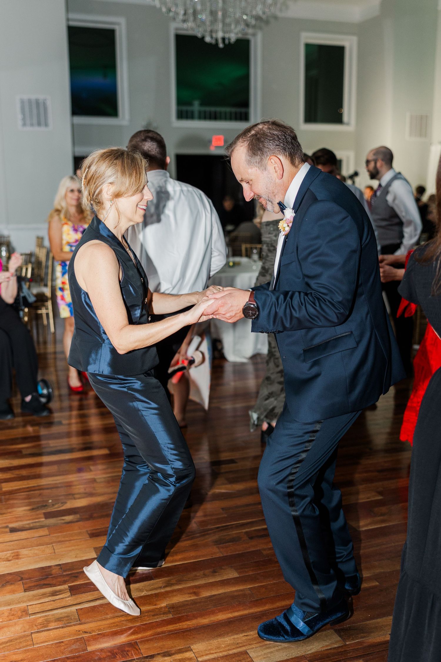 Wedding guests perform energetic dance moves on a polished hardwood floor during reception festivities.