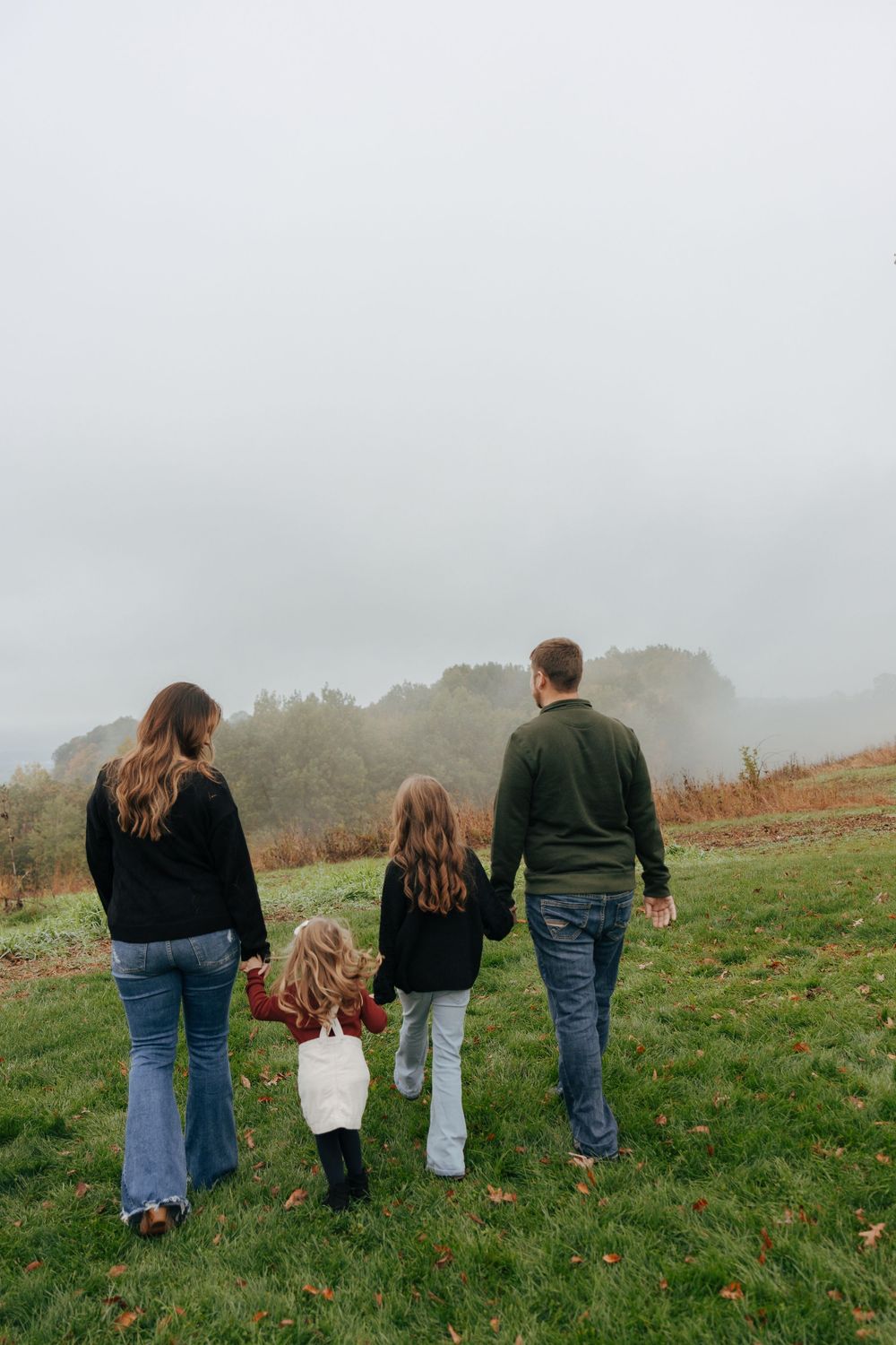 A family walks together on a misty hillside meadow in autumn.