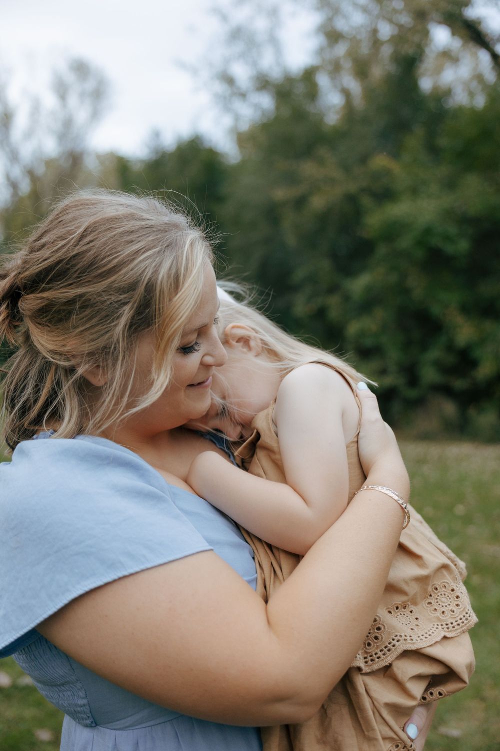 A tender moment between parent and child as they embrace outdoors in a natural setting with trees in the background.