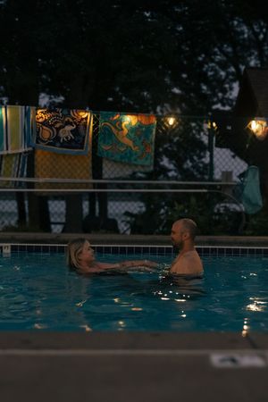 People swimming in an illuminated outdoor pool at dusk with trees visible in the background.