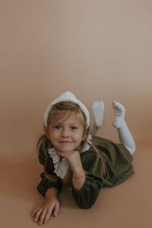 A child in an olive green dress lies on a beige floor in a series of playful poses.