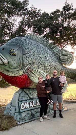 Large metallic fish sculpture serves as a roadside attraction in Onalaska with visitors posing next to it at sunset.
