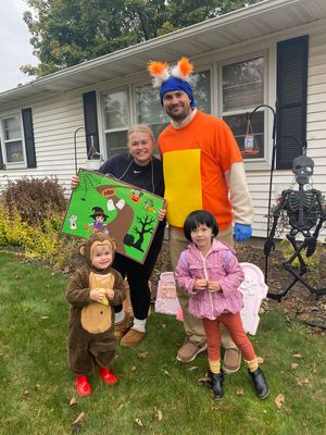 Children in Halloween costumes pose outdoors with adults on a fall day with autumn leaves on the ground.