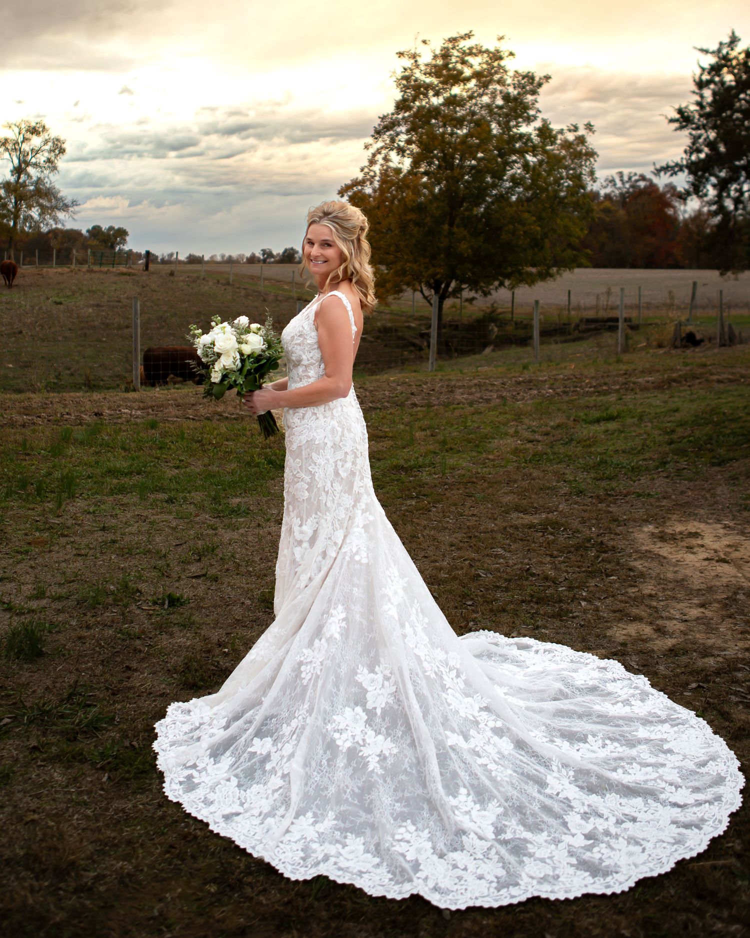 Stunning lace wedding dress with dramatic train photographed against rustic outdoor backdrop at sunset.