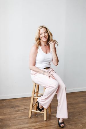 Fashion photo series showing someone in white tank top and pink pants posing casually on a wooden stool.