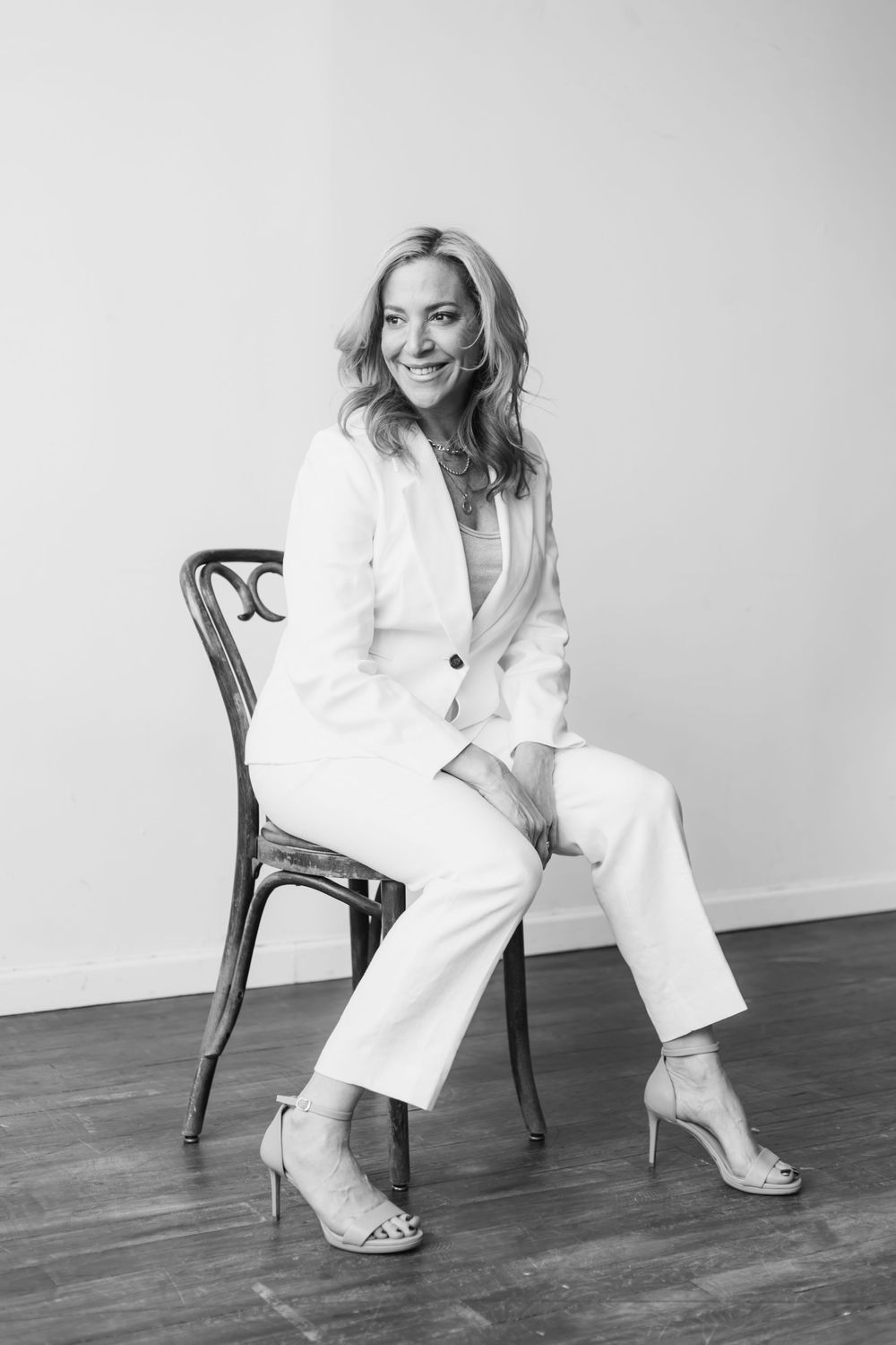 Black and white portrait series showing a person in a white suit sitting on a wooden chair in various poses.