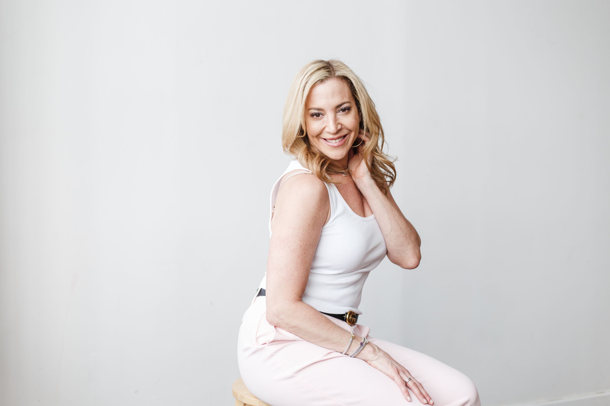 A woman in white athletic wear poses confidently against a light gray studio backdrop.