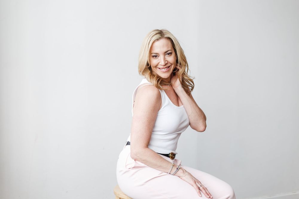A woman in white athletic wear poses confidently against a light gray studio backdrop.
