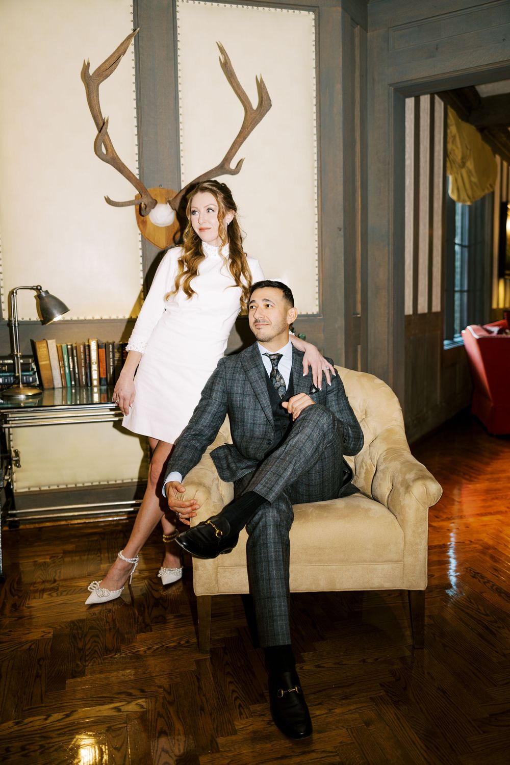 A couple in formal attire poses playfully in a series of shots on a couch in an elegant room with hardwood floors.
