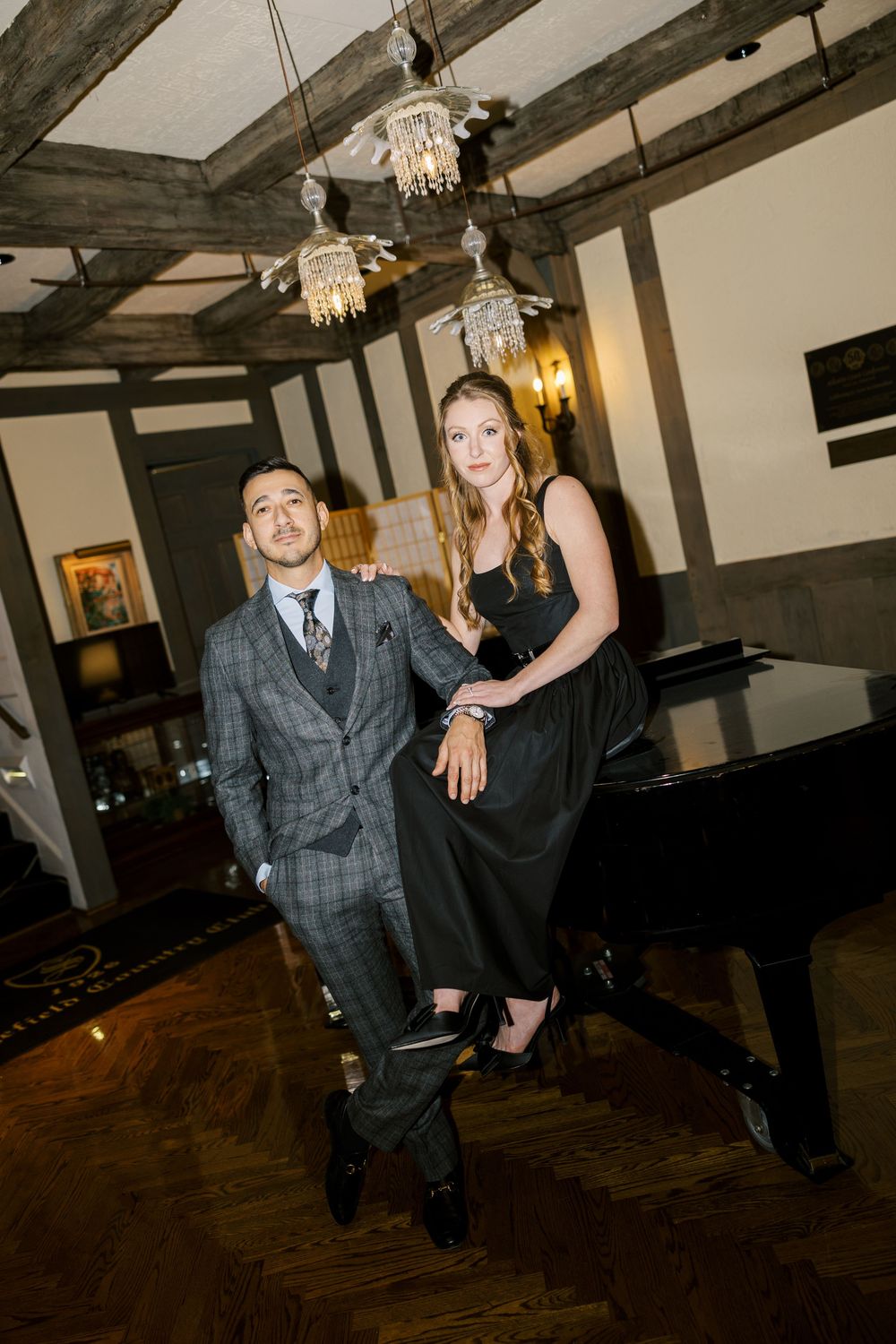 Wedding guests dance and celebrate on a dark wooden dance floor under crystal chandeliers in a rustic venue.