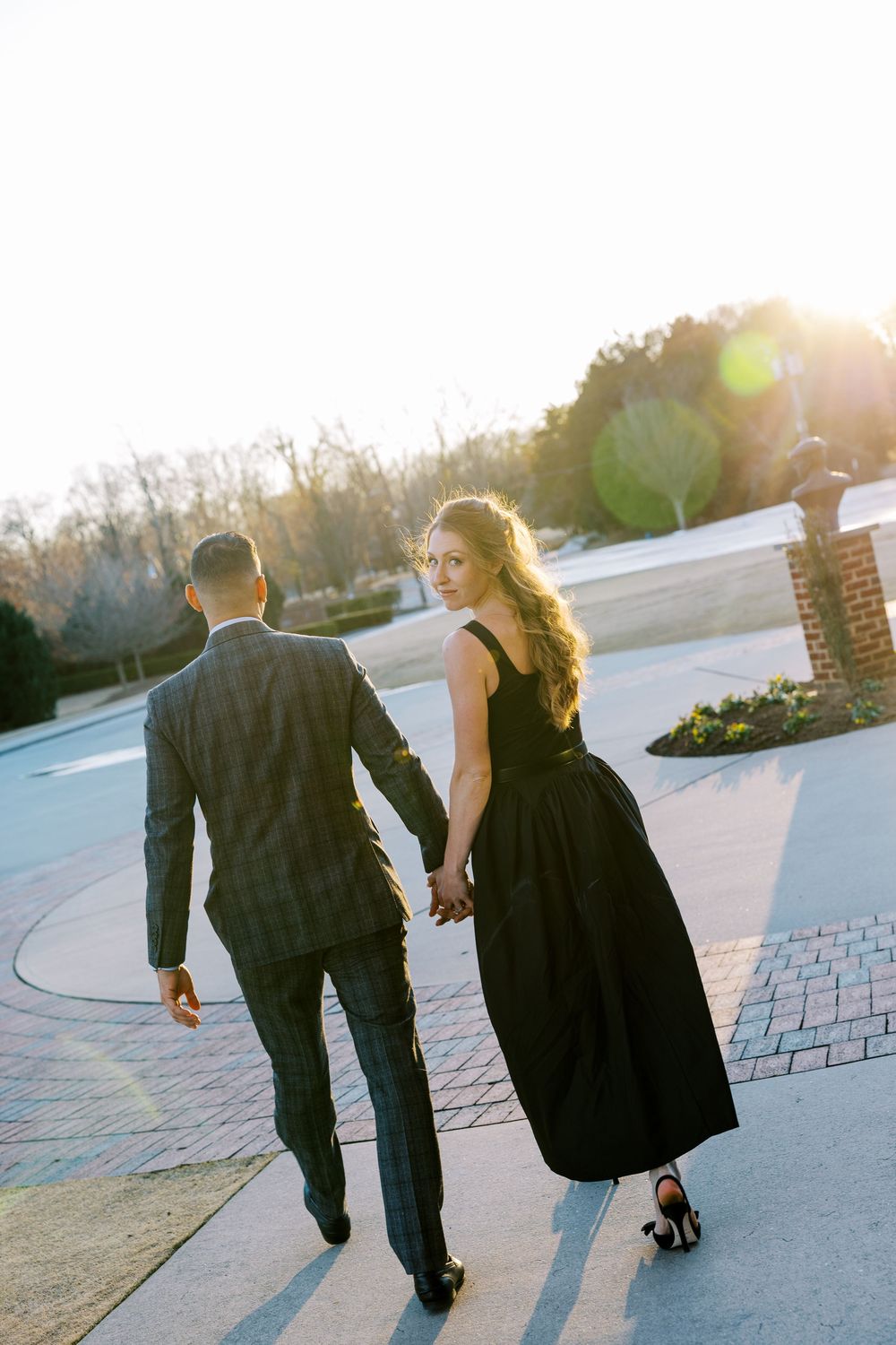 A couple walks hand in hand along a paved path during golden hour sunset, creating long shadows.