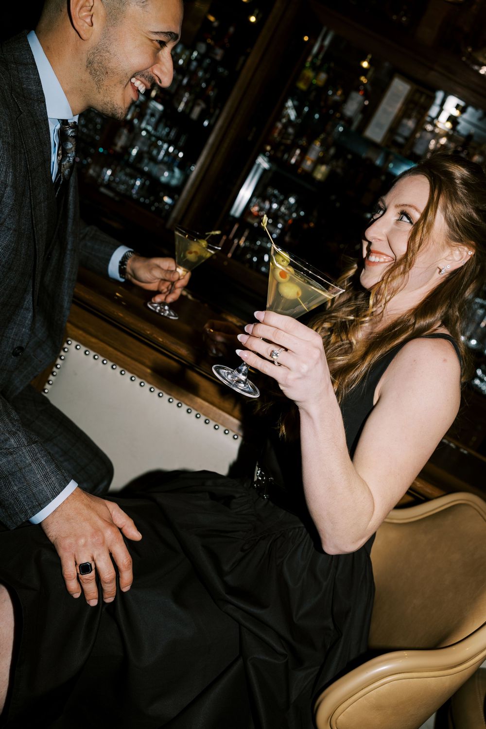A couple enjoying cocktails and conversation at an elegant bar with dark ambient lighting.