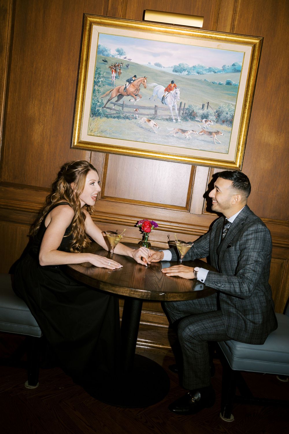 A romantic proposal moment unfolds in a dimly lit room with framed artwork on wood-paneled walls.