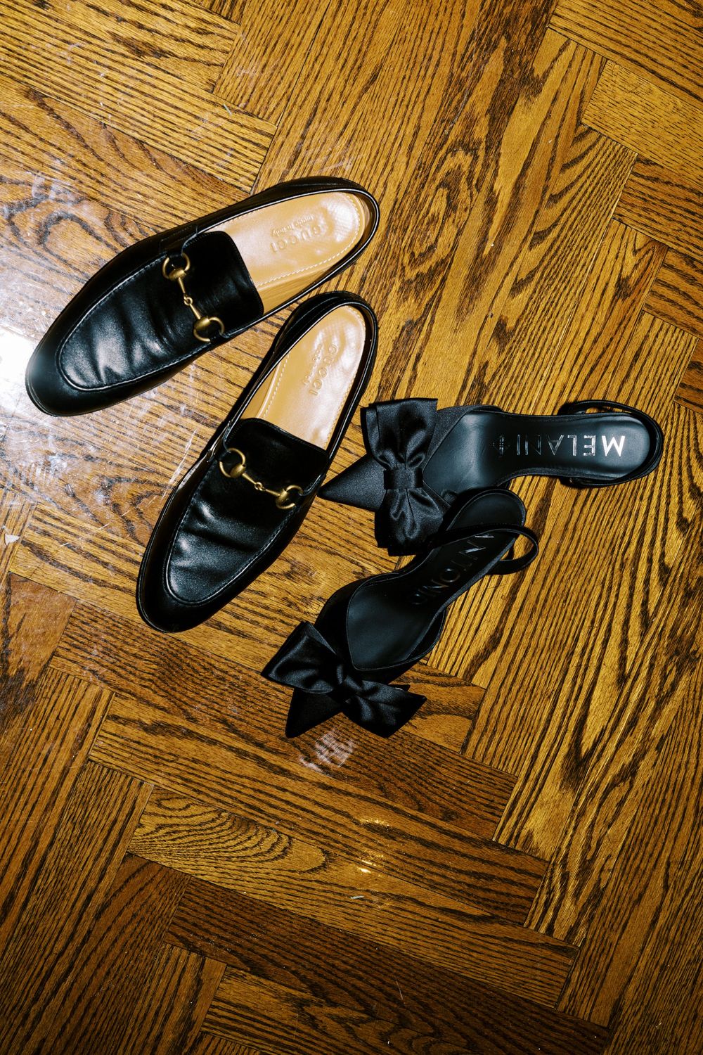 Black leather loafers and dress shoes arranged on a hardwood floor with warm oak grain pattern.