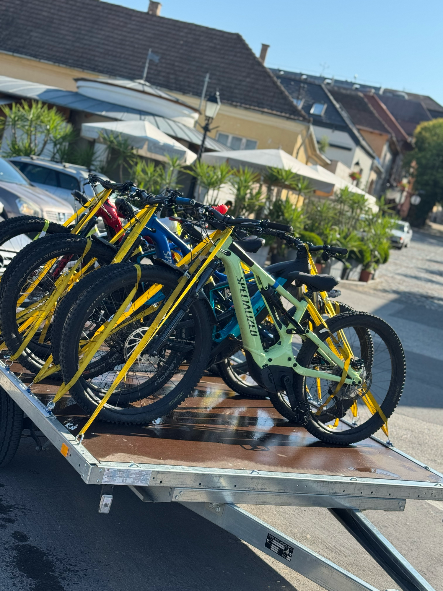 Several mountain bikes in yellow, blue and mint green colors loaded on a transport trailer in a residential area.