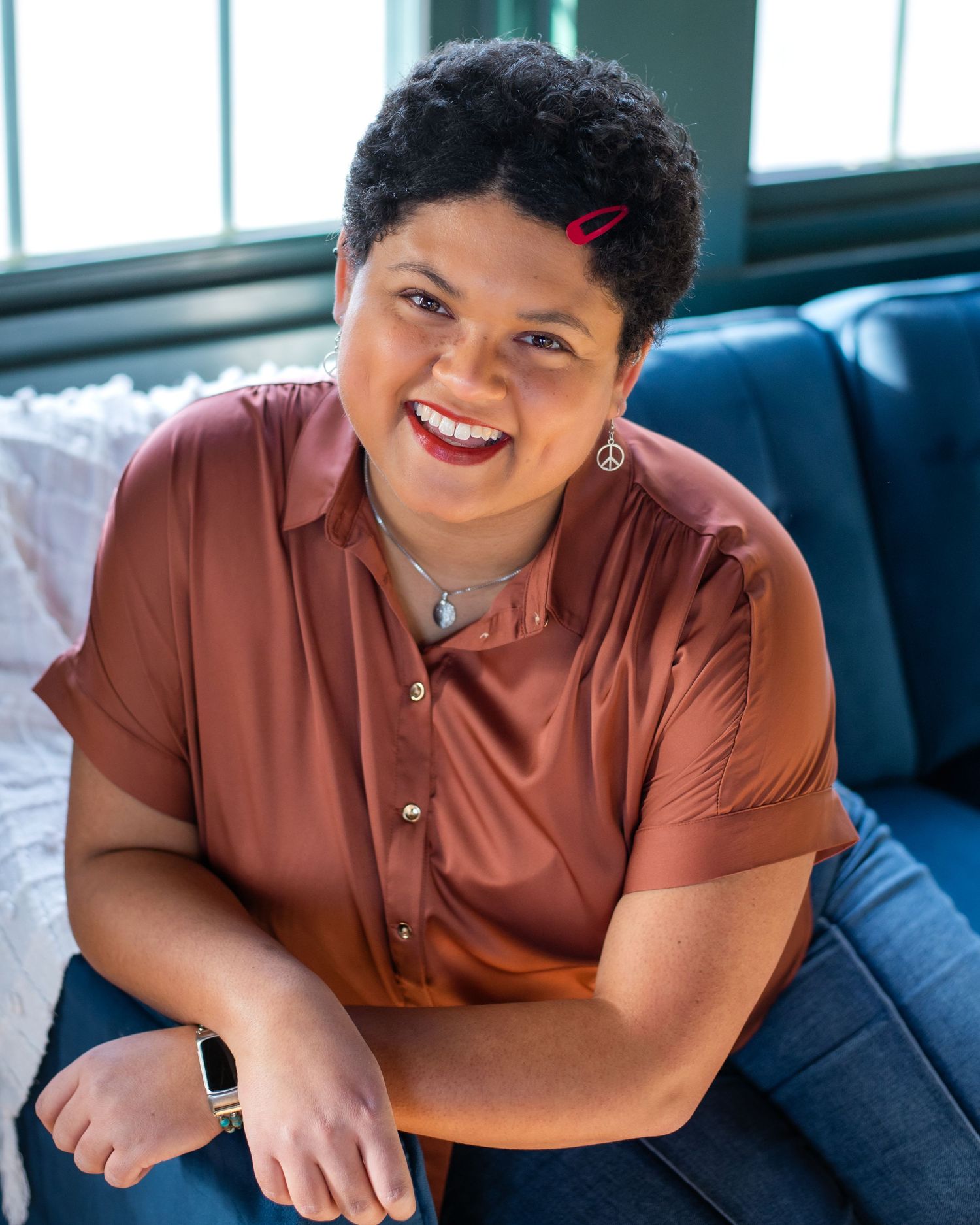 A person wearing a light blue sweater smiles warmly while sitting in a casual indoor setting.