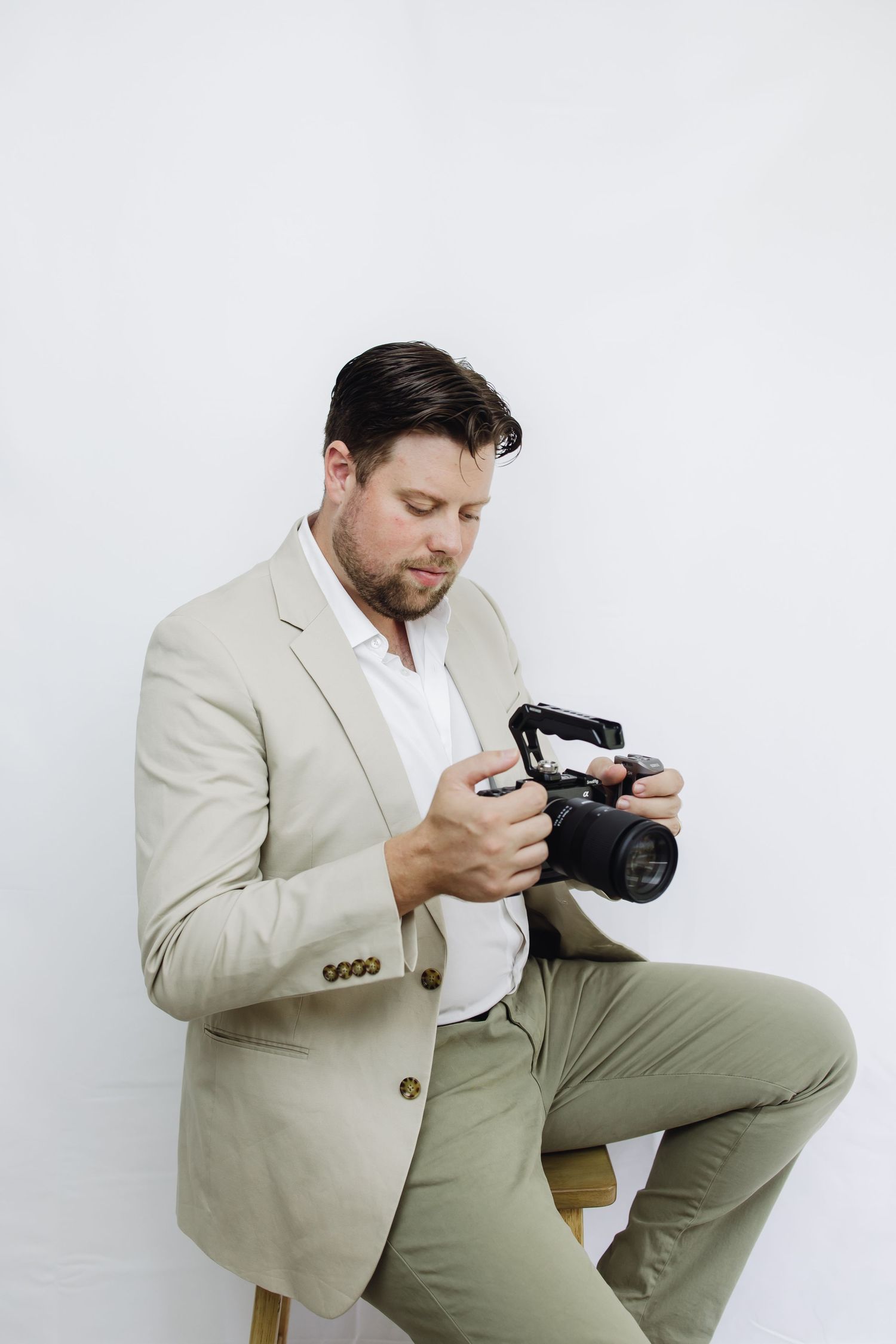 Professional photographer wearing beige blazer and olive pants examines camera settings in studio sequence.