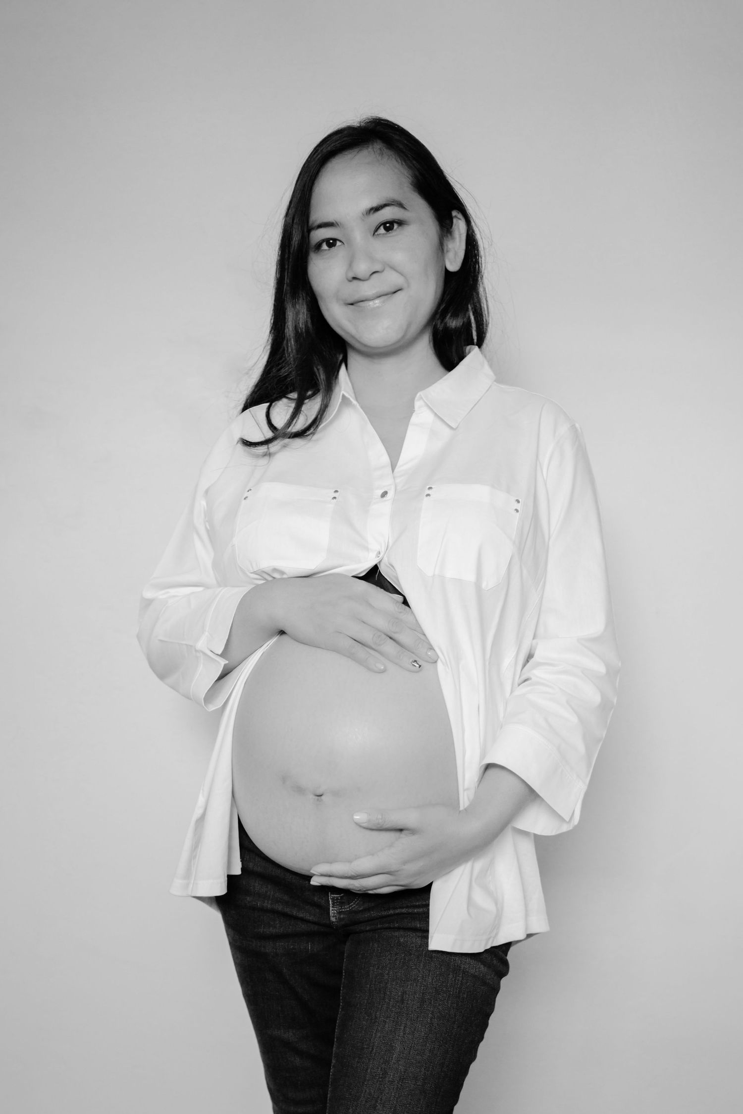Pregnant woman wearing a white shirt opened to expose her belly. (black and white) In-home maternity session.  Doughman Photography