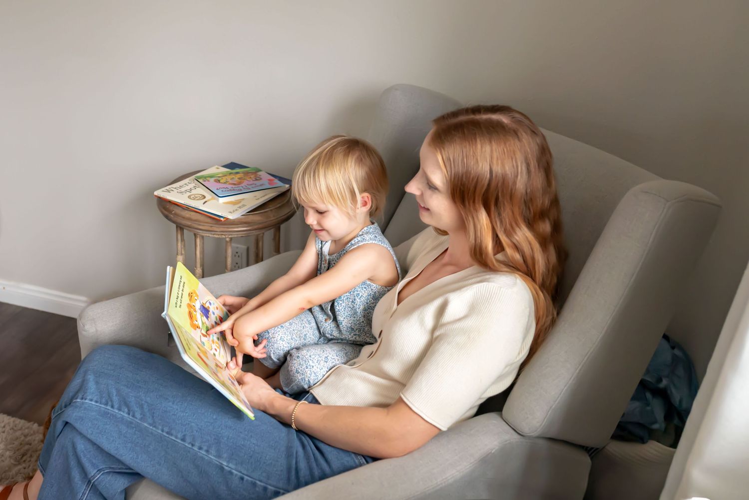 Mom reading to her little girl in an arm chair. The child points to an image in the book. Doughman Photography