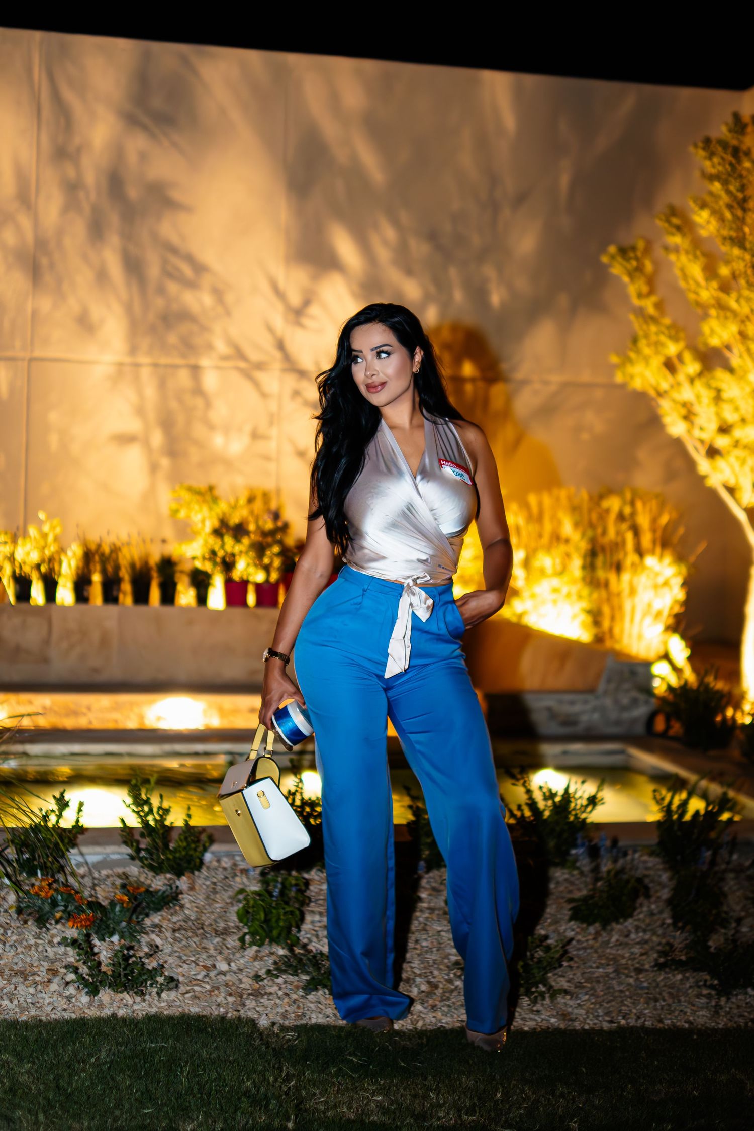 Fashionable outfit featuring bright blue wide-leg pants and white crop top against warm evening garden lighting.