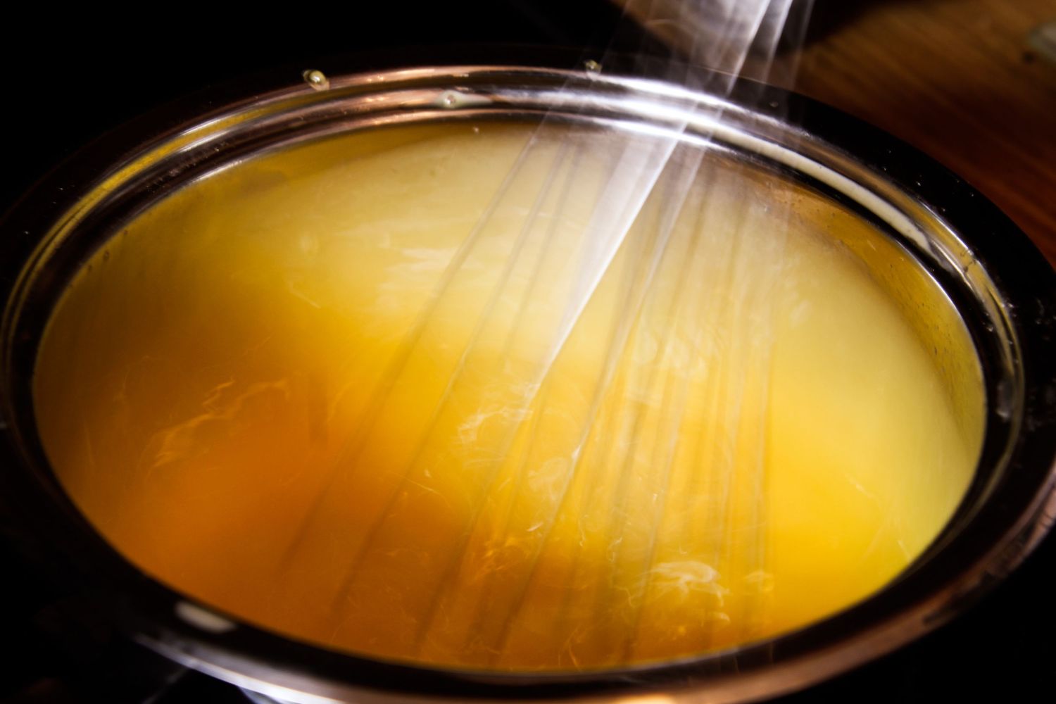 Steaming yellow broth or soup viewed from above in a dark bowl with dramatic lighting.