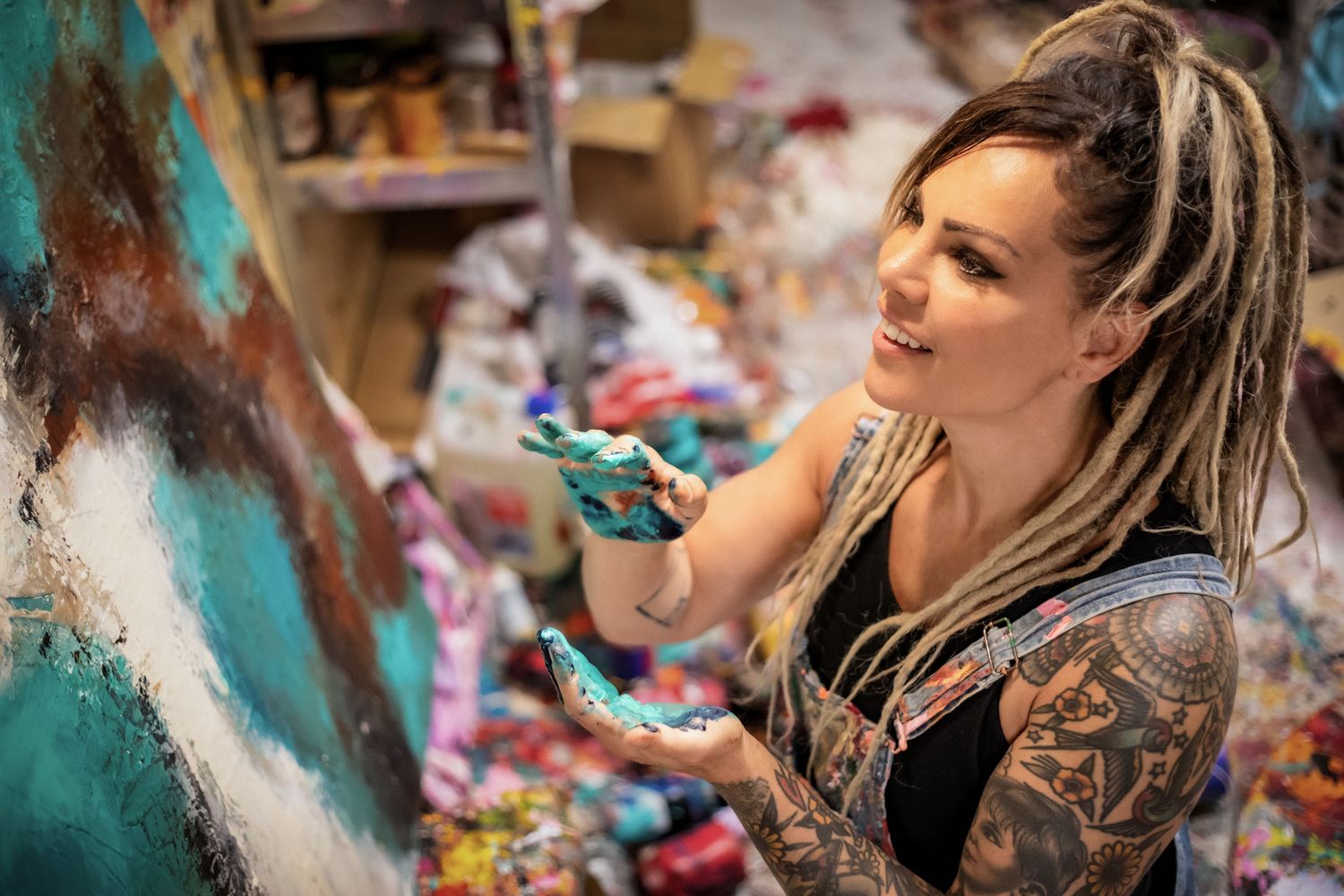 Creative artist with dreadlocks concentrates while painting in their art studio surrounded by supplies.
