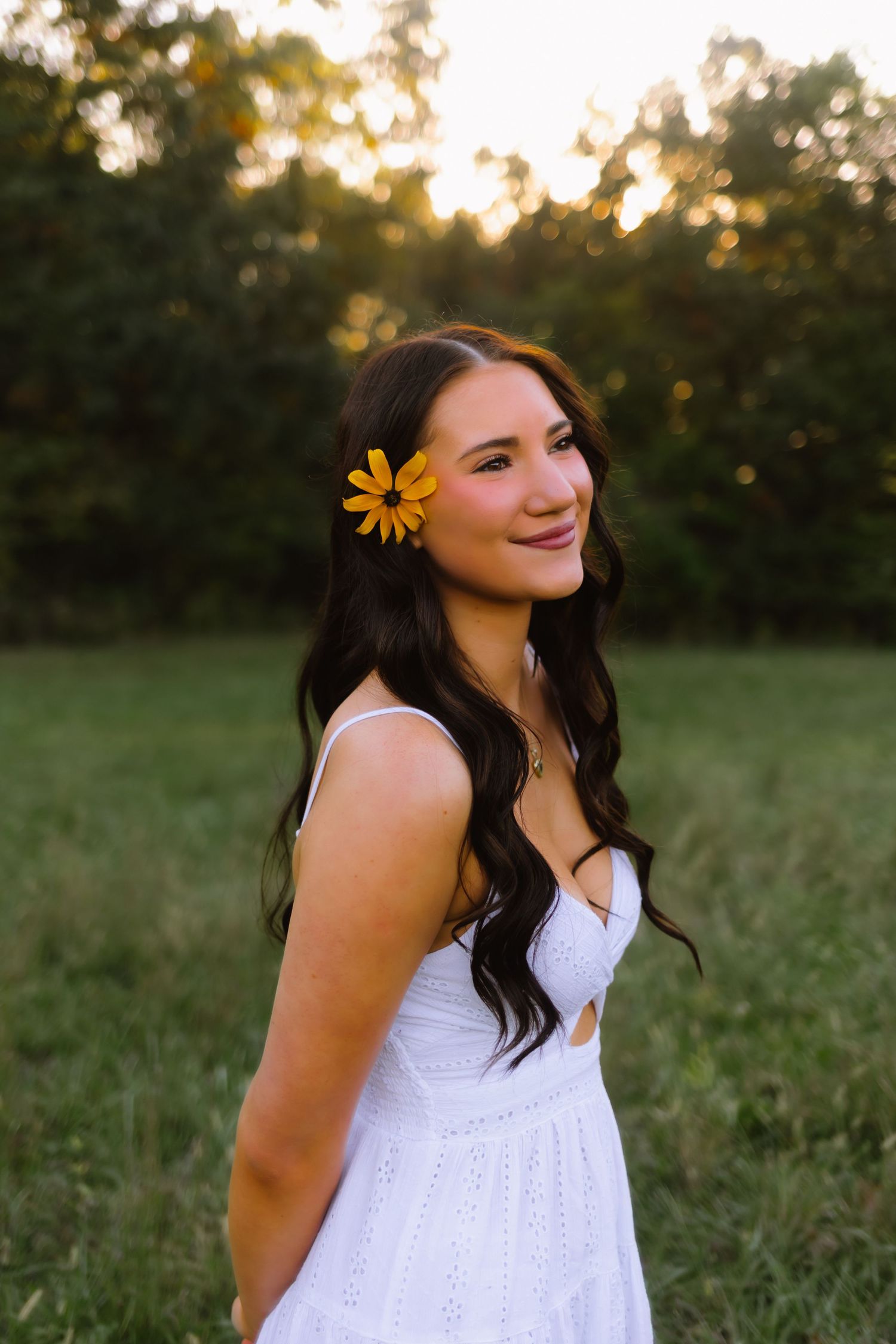 Woman in teal dress holding bouquet while posing on sidewalk near trees.